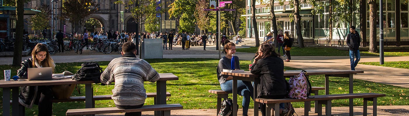 Students sitting on a bench in Brunswick Park on The University of Manchester campus